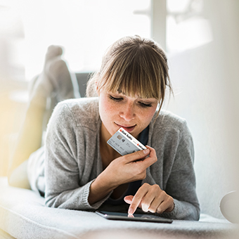 Eine Frau liegt auf dem Sofa vor ihrem Laptop mit der Debitkarte in der Hand