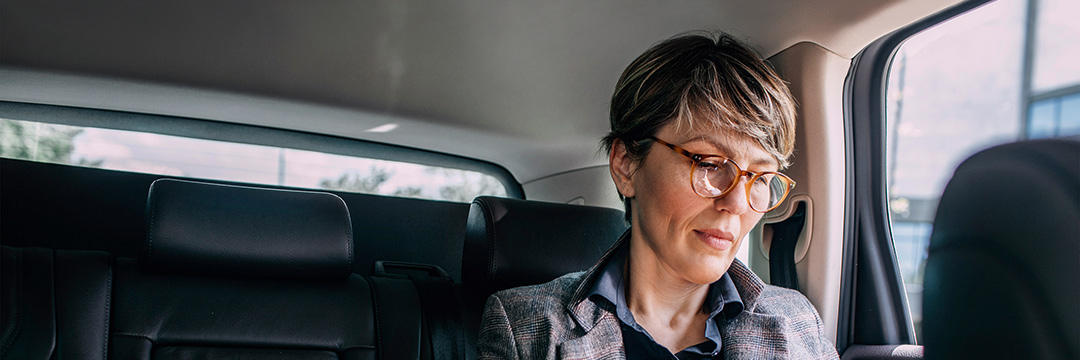 Eine Frau sitz auf der Rückbank eines Autos und schaut auf ihr Handy