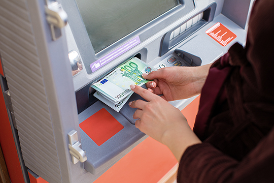 Jemand behebt Geld bei einem Geldausgabeautomaten
