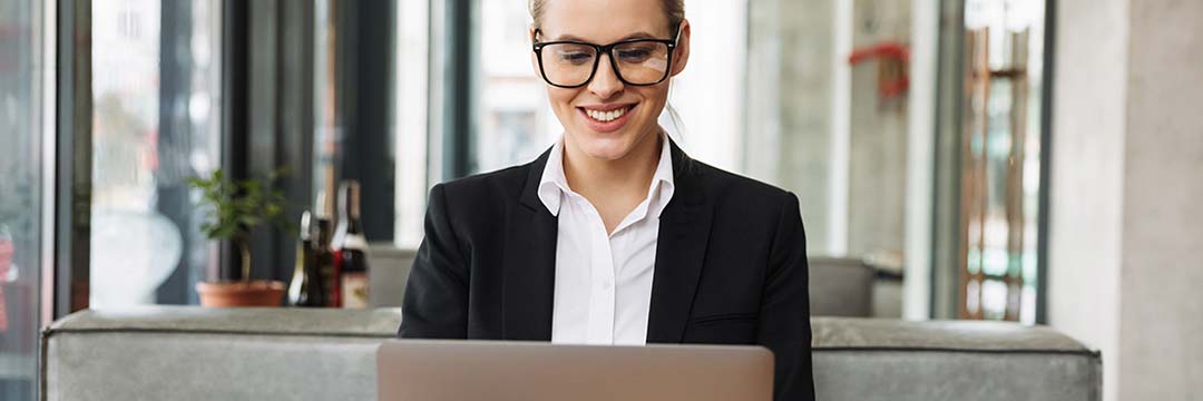 Smiling blonde business woman sitting by the table in cafe and using laptop computer