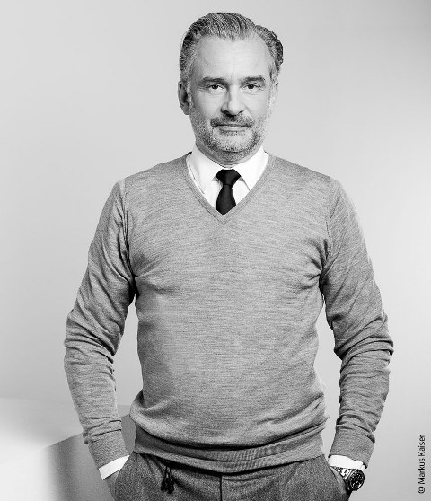 Architekt Stephan Ferency in Frontalansicht, er trägt einen grauen Pullover und ein weißes Hemd mit Krawatte.