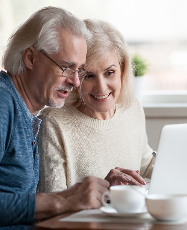 Eine ältere Frau und ein älterer Mann sitzen vor dem Laptop