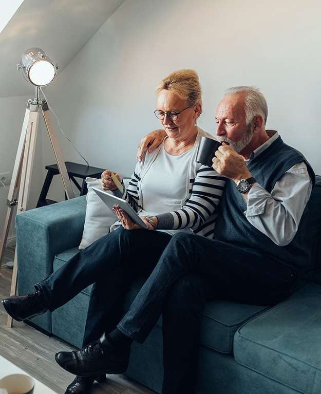 älterer Mann und ältere Frau sitzen mit einem Tablet gemeinsam auf der Couch