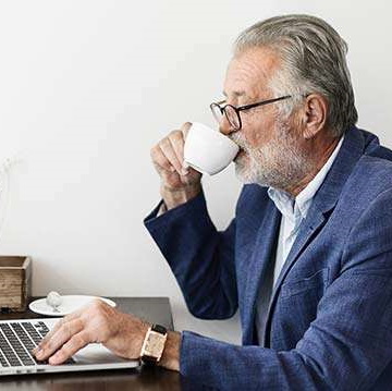 Ein Mann trinkt aus einem Glas und schaut auf einen Laptop