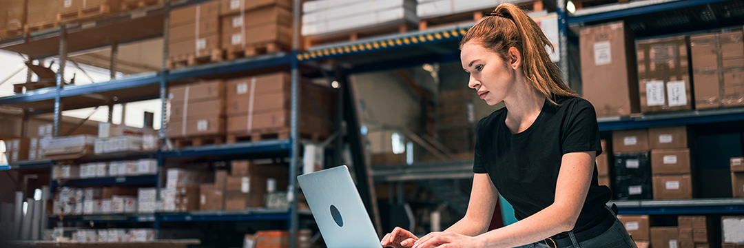 Eine Frau steht in einer Lagerhalle vor dem Laptop