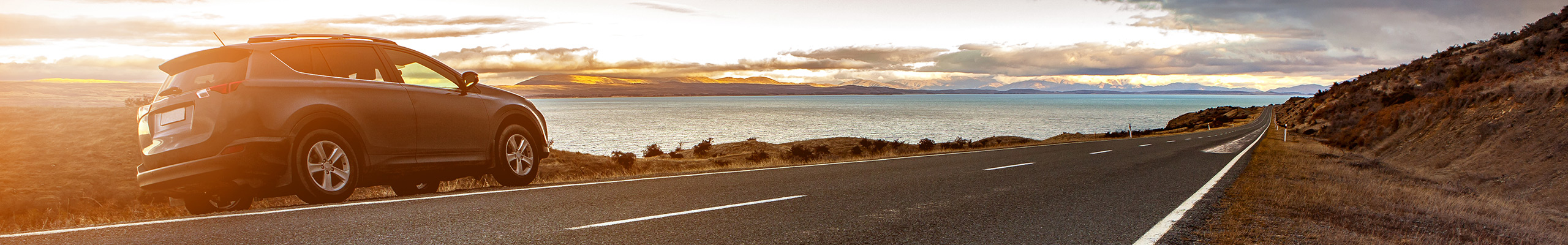 Ein Auto steht am StraÃenrand vor dem Meer im Sonnenuntergang