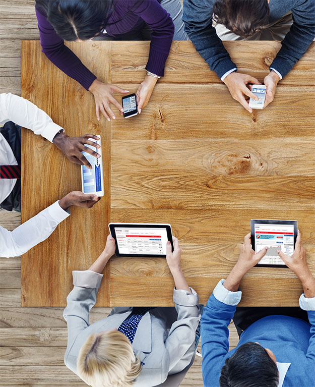 Eine Gruppe von Menschen sitzen um einen Tisch herum und schauen auf Ihr Tablet oder Smartphone