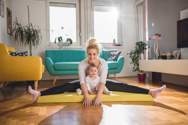 eine Frau macht mit ihrem Kleinkind Turnübungen im Wohnzimmer