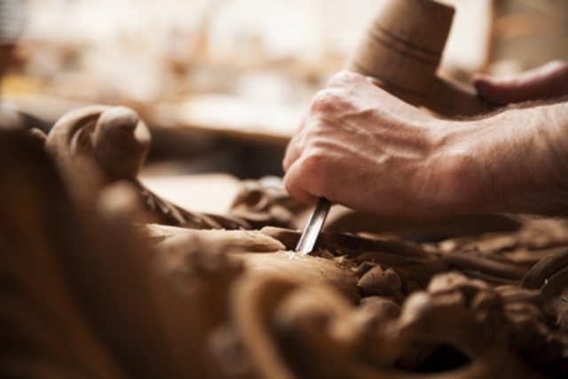 Eine Hand schnitzt ein Muster in Holz.