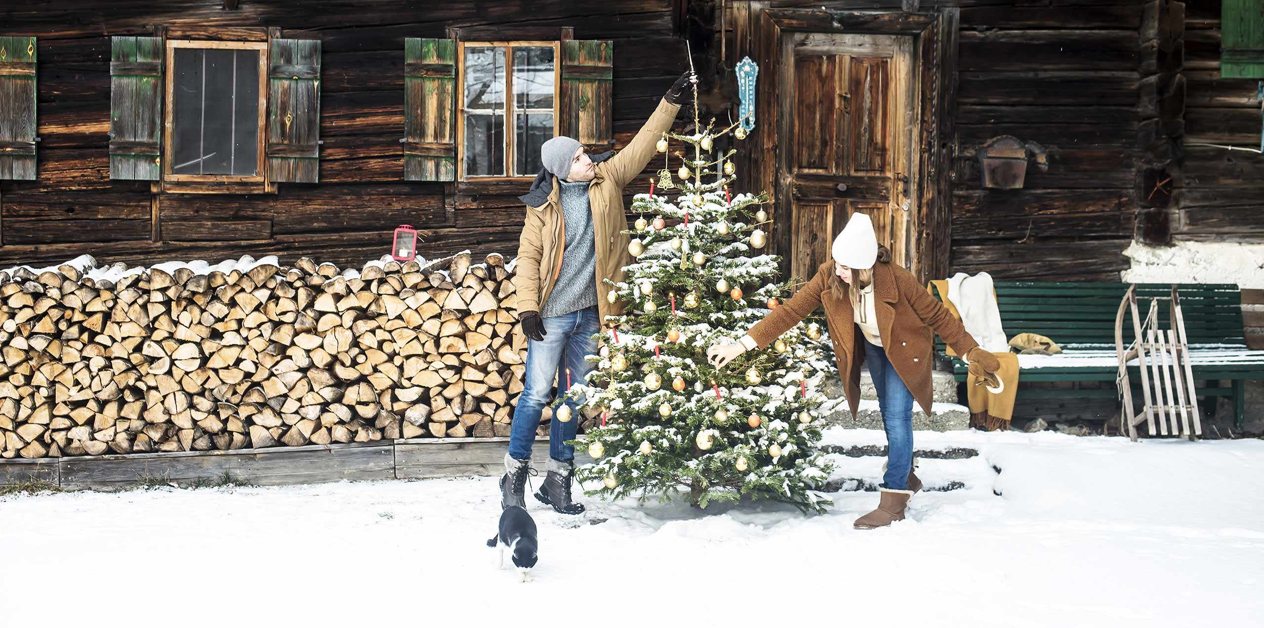 A couple decorates a christimas tree in front of a house in the snow