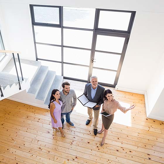 Eine Immobilienmaklerin und ein Immobilienmakler zeigen einem jungen Pärchen ein helles offenes Haus