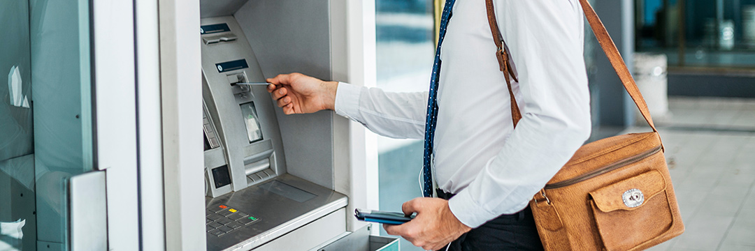 Ein Mann steht vor einem Bankomaten und führt eine Bankomatkarte ein.