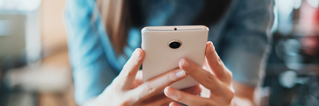 Eine Frau hält ein Smartphone mit beiden Händen und schaut darauf