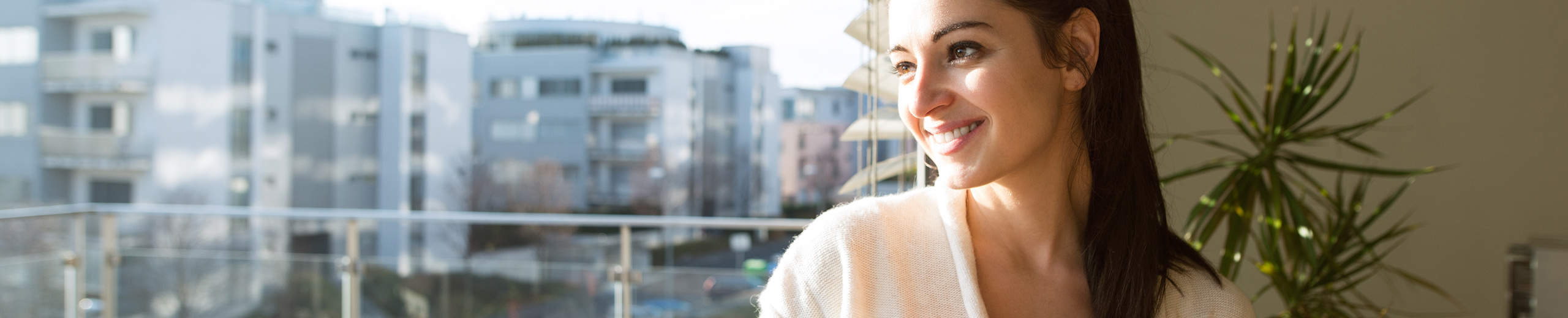 Frau steht auf einem Balkon, im Hintergrund sieht man Hochhäuser